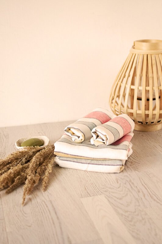 Off white heavy linen towels for hands, face or guests, to use in the bathroom. Off white towels are with pastel colors stripes.