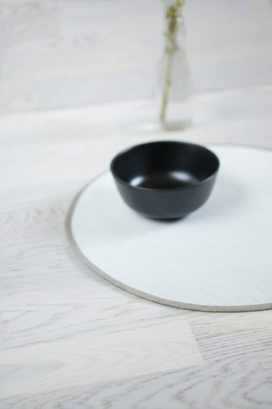 Round linen placemats with a reversible design, one side off-white and the other natural linen, with a natural linen border.