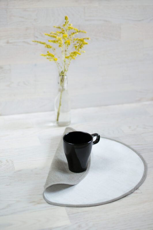 Round linen placemats with a reversible design, one side off-white and the other natural linen, with a natural linen border.