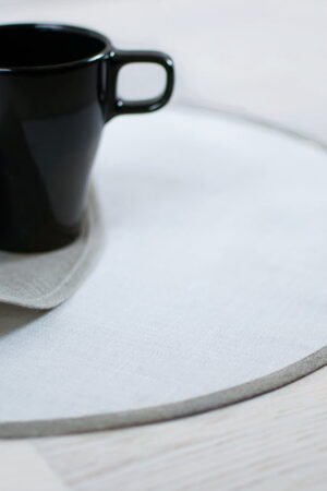 Round linen placemats with a reversible design, one side off-white and the other natural linen, with a natural linen border.