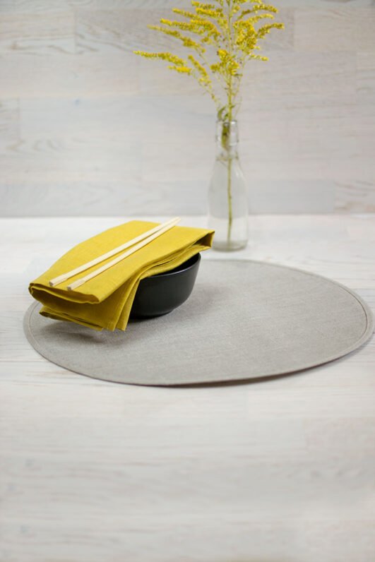 Round linen placemats with a reversible design, one side off-white and the other natural linen, with a natural linen border.