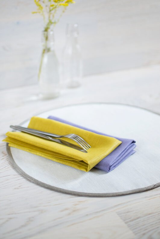 Round linen placemats with a reversible design, one side off-white and the other natural linen, with a natural linen border.