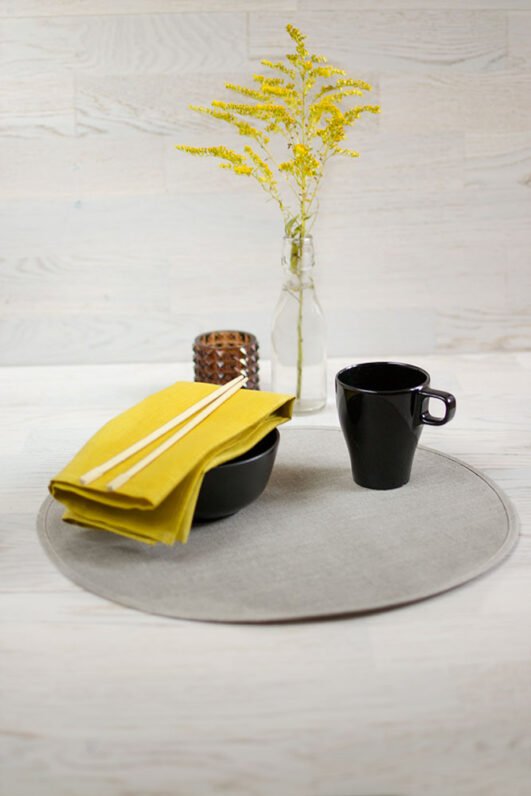 Round linen placemats with a reversible design, one side off-white and the other natural linen, with a natural linen border.