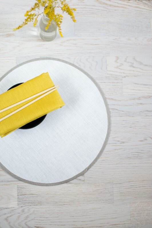 Round linen placemats with a reversible design, one side off-white and the other natural linen, with a natural linen border.