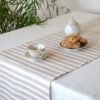 Short natural striped linen table runner with stripes goes across the runner.