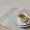 Light natural linen placemat with off-white lace trim, elegant table setting.
