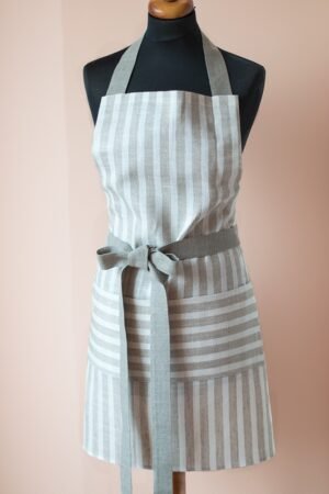Striped linen apron with adjustable belt and pocket. Stipes goes along the apron natural linen color with off white. Belt made from natural linen. And the apron's pocket made from the stipes goes across the apron.