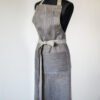 Grey linen apron made from melange linen - black with natural linen yarns. The belt is adjustable and made from natural linen. One big pocket on front.
