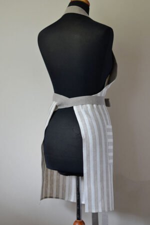 Striped linen apron with adjustable belt and pocket. Stipes goes along the apron natural linen color with off white. Belt made from natural linen. And the apron's pocket made from the stipes goes across the apron.