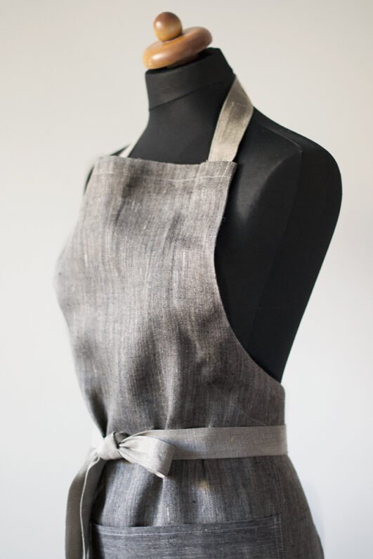 Grey linen apron made from melange linen - black with natural linen yarns. The belt is adjustable and made from natural linen. One big pocket on front.
