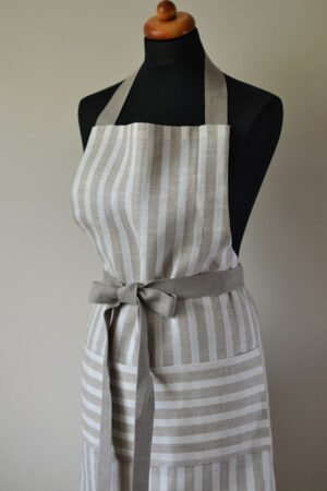 Striped linen apron with adjustable belt and pocket. Stipes goes along the apron natural linen color with off white. Belt made from natural linen. And the apron's pocket made from the stipes goes across the apron.