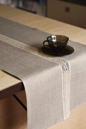 Natural tan linen table runner with a decorative linen lace trim through the middle.