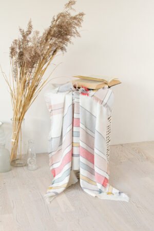 Soft linen blanket in off-white with colorful stripes used as a sofa cover. This versatile sofa throw blanket features decorative fringes on two edges, perfect for cozy home decor.