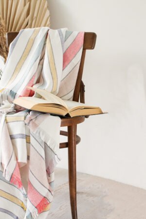 Soft linen blanket in off-white with colorful stripes used as a sofa cover. This versatile sofa throw blanket features decorative fringes on two edges, perfect for cozy home decor.