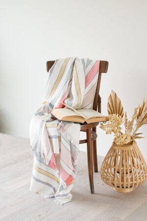 Soft linen blanket in off-white with colorful stripes used as a sofa cover. This versatile sofa throw blanket features decorative fringes on two edges, perfect for cozy home decor.
