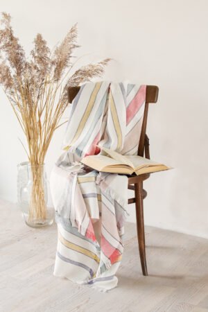 Soft linen blanket in off-white with colorful stripes used as a sofa cover. This versatile sofa throw blanket features decorative fringes on two edges, perfect for cozy home decor.