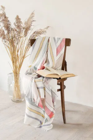 Soft linen blanket in off-white with colorful stripes used as a sofa cover. This versatile sofa throw blanket features decorative fringes on two edges, perfect for cozy home decor.